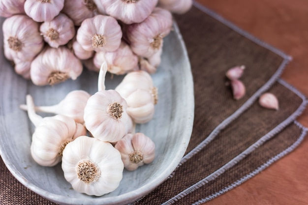 Garlic cloves on calico tablecloth and Garlic bulb in vintage ceramic bowl on wood.