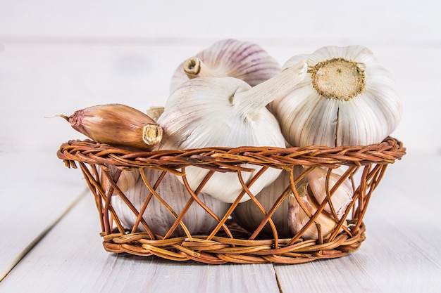 Garlic cloves and garlic bulb in a basket on a white wooden table.