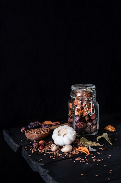 暗い素朴な表面のニンニク、ドライフルーツ、種子。低キーciaroscurroスタイルで撮影した古い黒いテーブルの上の瓶にニンニクとドライフルーツの芸術的な写真