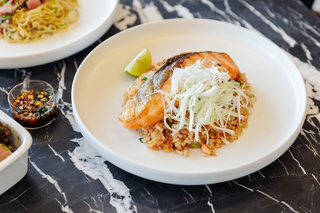 Garlic fried rice with grilled salmon served with chili bean sauce on black marble top table.