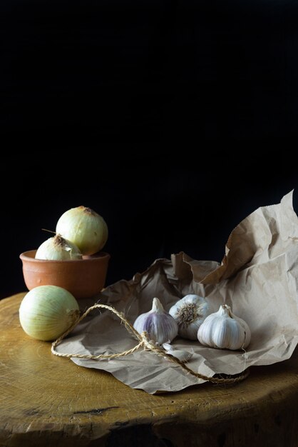 Garlic and onions, garlic and onions placed on brown paper over rustic wood, small depth of field, black background, selective focus.