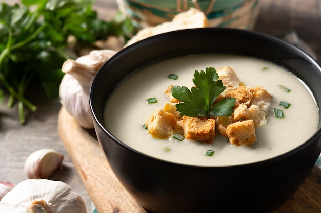 Garlic soup topped with croutons in bowl on wooden table