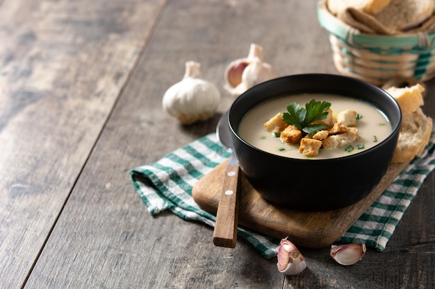 Garlic soup topped with croutons in bowl on wooden table