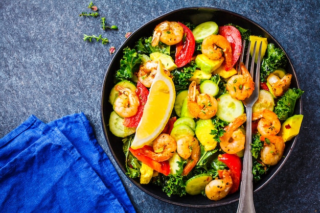 Garnalen, avocado en plantaardige salade in een zwarte schotel op blauwe achtergrond, hoogste mening.