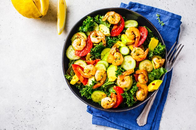 Garnalen, avocado en plantaardige salade in een zwarte schotel op grijze achtergrond, hoogste mening.