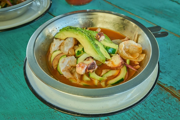 Garnalen in aguachile geserveerd op een metalen plaat op een blauwgroene achtergrond