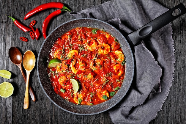 Garnalen karahi - pakistaanse tomaat garnalen curry met limoensap rode chili en rode curry pasta geserveerd op een koekenpan met verse koriander op een donkere houten achtergrond met linnen handdoek, bovenaanzicht, close-up