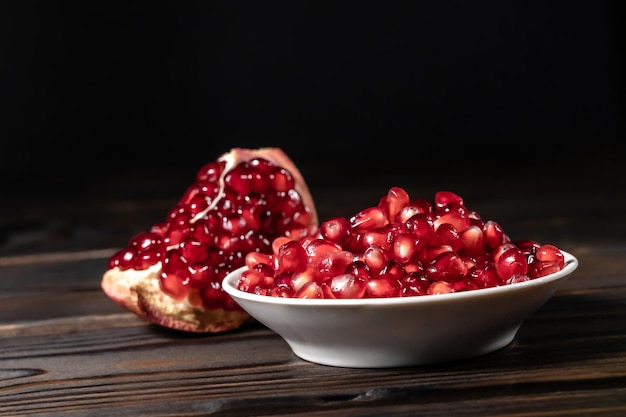 Garnet seeds in white plate and cracked pomegranate on wooden background