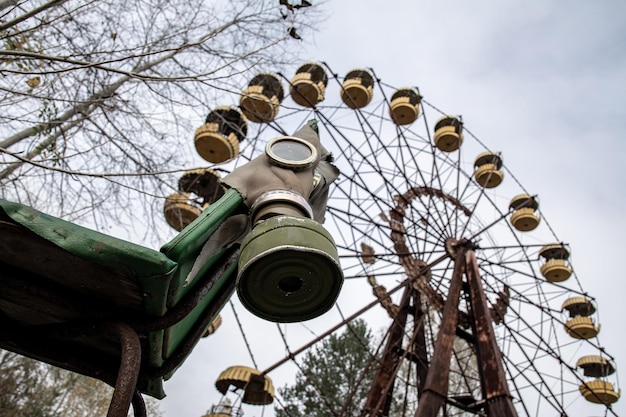 Gas mask holding on old chair ferris wheel on background\
pripyat ghost city chernobyl 30 km