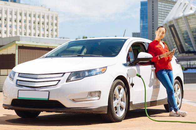 Gas station. Confident pleasant woman standing near her car while being at the gas station