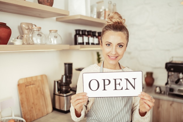 Gasten verwelkomen. Mooie eigenaar van een kleine coffeeshop met een bordje met de tekst 'open'.