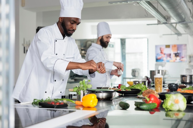 Gastronomie-expert die kookuniform draagt terwijl hij een heerlijk gastronomisch gerecht bereidt voor het diner in het restaurant. Chef-kok met pan op gasfornuis tijdens het koken van een smakelijke maaltijd in de keuken.