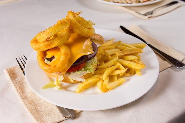 Gastronomische cheeseburger en frietjes op bord bij couvert op tafel