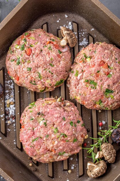 Gastronomische creatie bovenaanzicht van rauwe Hamburger pasteitjes met kruiden sissend in een gietijzeren pan in afwachting