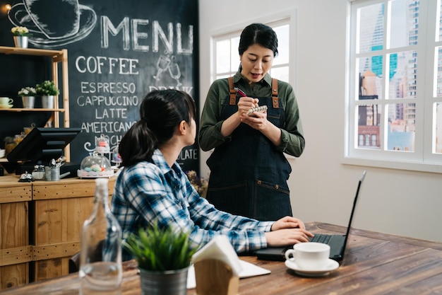 Gastvrije serveerster met briefpapier en potlood klaar om de bestelling van de klant op te nemen. vrouwelijke freelancer werknemer in coffeeshop begint haar werkdag met laptopcomputer binnenshuis. jong meisje personeel herhaal maaltijd?