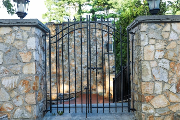 A gate with a stone wall and a stone wall with a fence and trees in the background.