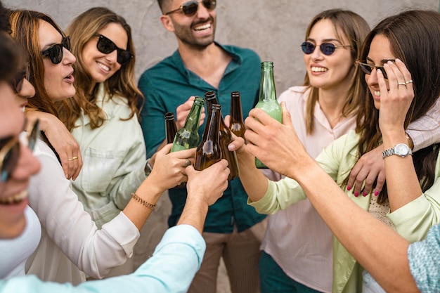 Gathering of happy young people toasting with bottled beers clinking together outdoors - friends having fun drinking alcoholic drinks concept