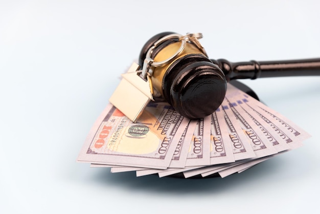 Gavel on top of pile of money and house model on blue background