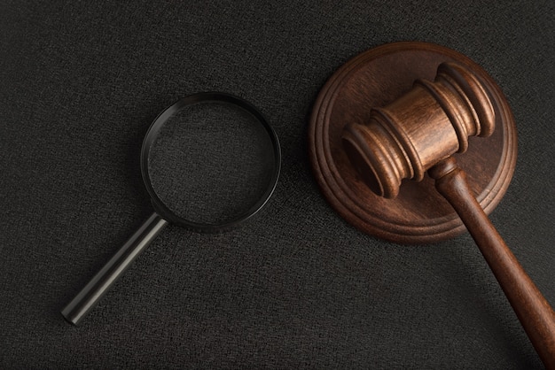 Gavel with magnifying glass on black background. Forensic investigation. Collection of evidence. Jurisprudence concept.