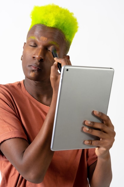 A gay black man putting on makeup LGTBI concept correcting blemishes with a mirror