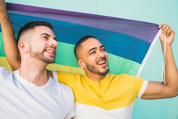 Gay couple embracing and showing their love with rainbow flag.