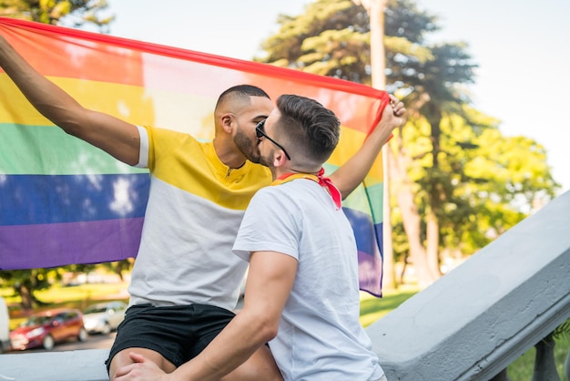 Photo gay couple embracing while holding flag standing outdoors