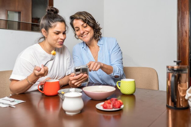 Gay couple having breakfast while watching the mobile and laughing together