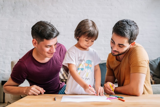 Gay couple having fun with their son while drawing something on a paper at home. Family concept.