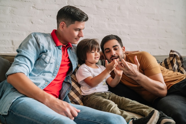 Gay couple having fun with their son while spending time together on a couch at home. Family concept.