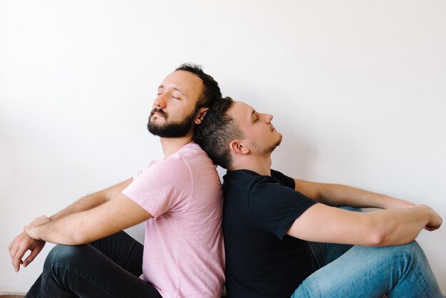 Photo gay couple sitting back-to-back at home