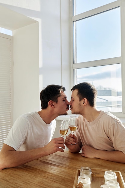 Гомосексуальная пара с вином, целующаяся с закрытыми глазами.