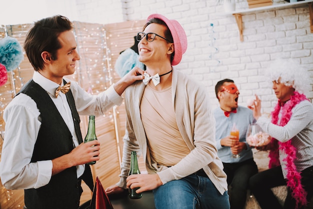 Gay guy touching bow tie of another man at party.