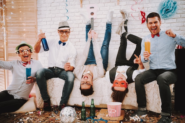 Gay guys in bow ties playfully posing on couch at party.