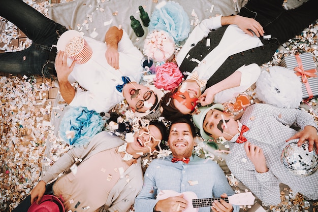 Gay guys lying in circle with confetti at party.