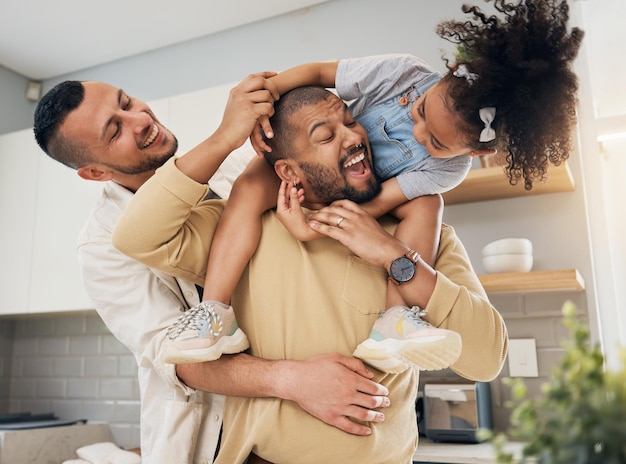 Gay happy family and playing with child in home or parents together with love support and girl on shoulders of dad LGBT fathers and men with happiness smile and fun bonding in kitchen with kid