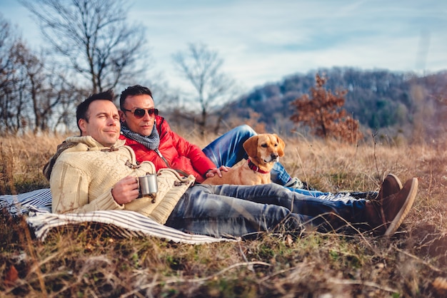 Gay male couple laying on blanket in grass with dog