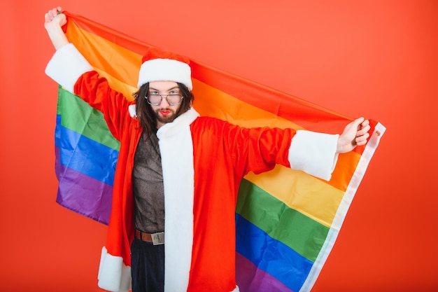 Gay Man dressed as Santa Claus holding a multicolored flag