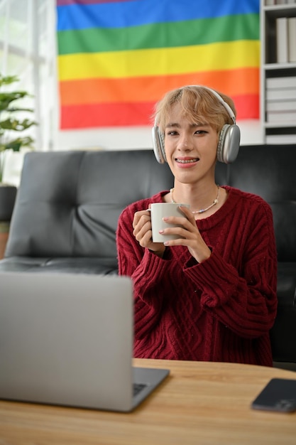 A gay man freelancer is working from home holding a coffee mug and listening to music