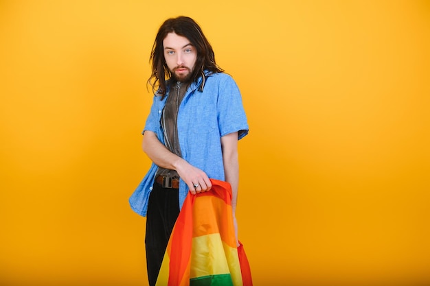 ゲイの男性は、色付きの背景のスタジオ ポートレートの人々 のライフ スタイル ファッション lgbtq コンセプトに分離されたレインボー ストライプ フラグを保持します。
