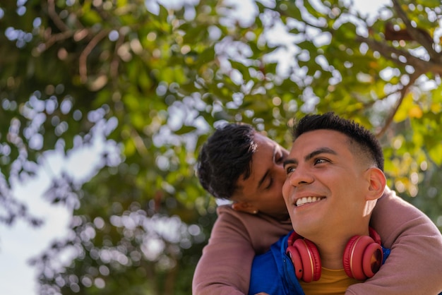 Gay man riding piggyback and kissing his partner outdoors