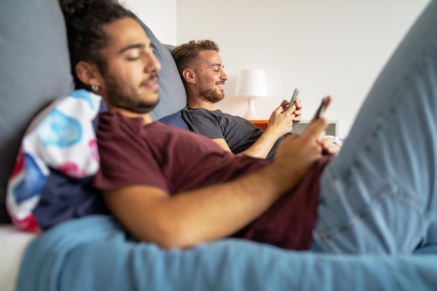 Foto gay paar met behulp van smartphone digitale apparaten liggend op het bed. homoseksueel paar die thuis op sociale media letten