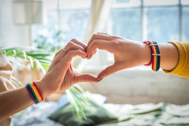 Mani femminili di concetto di orgoglio gay che fanno un segno del cuore con braccialetto con bandiera arcobaleno lgbt gay pride