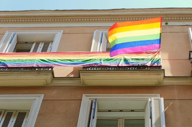 LGBTフレンドリー地区チュエカのマドリッドスペインのダウンタウンにあるゲイプライドフラッグバックライト付きサンファサードビル
