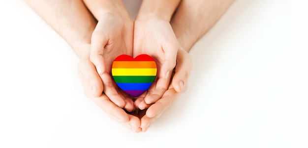 gay pride, homosexual, love and charity concept - close up of male and female hands holding small rainbow heart