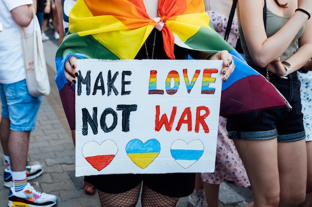 Gay pride LGBTQ solidariteitsmars met regenboogvlaggen en anti-oorlogse posters Handen met een poster met Make love not war