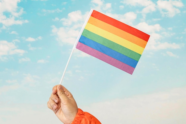 Gay pride rainbow flag fluttering backlit in the sun against soft blue sky