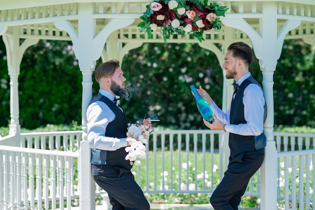 パートナーとゲイのカップルが結婚式中に一緒に花束を持ってシャンパンを開く