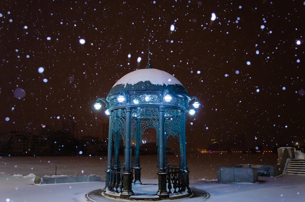 Gazebo gemaakt van metaal in de winteravond in een sneeuwval.