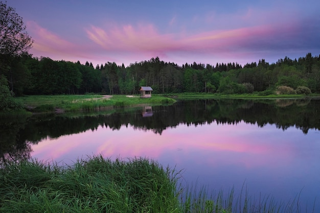 Gazebo on the shore of a forest lake at sunset, in summer