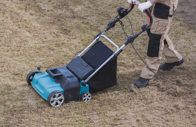 Gazon verticuteren met een verticuteermachine. Man tuinman verticuteert het gazon en verwijdert oud gras